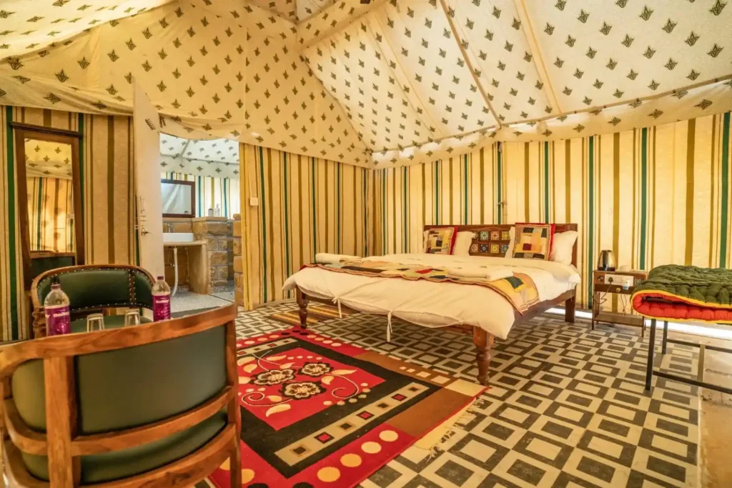 Bedroom inside a striped canvas tent with a queen bed, patchwork pillows, and a bold red geometric rug.