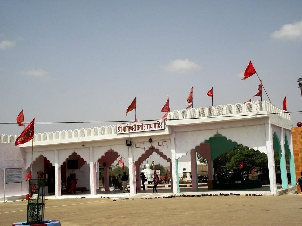 White temple entrance with decorative arches, red flags atop, and a sign in Hindi above the gate.