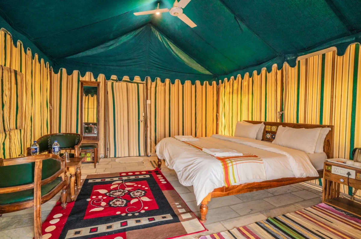 Glamping tent interior with a wooden king bed, white bedding, striped yellow-green walls, and a ceiling fan above.