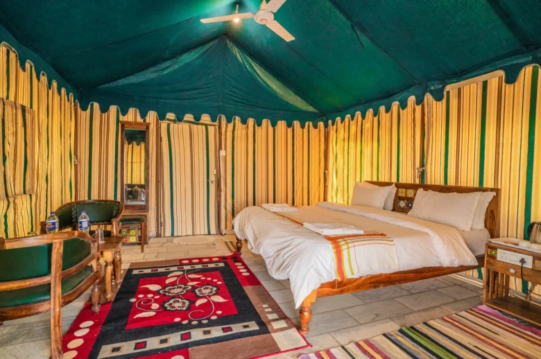 Glamping tent interior with a wooden king bed, white bedding, striped yellow-green walls, and a ceiling fan above.